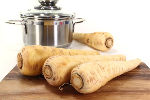 fresh parsnips on wooden board with a pot on light background