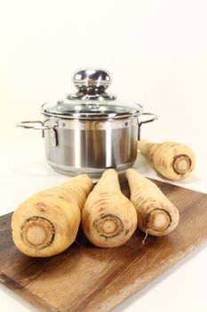 parsnips on wooden board with a pot on light background