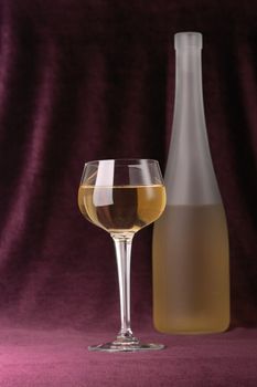 Glass and bottle of white wine on a background of an elegant velveteen material of claret color