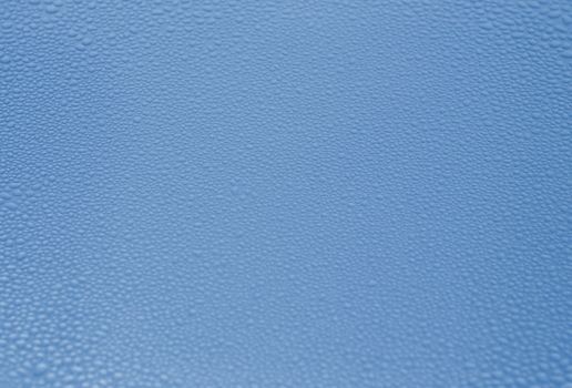 Fine transparent drops of rain water or condensate on a rough blue metal surface