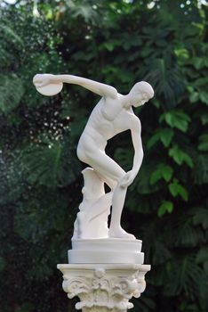 The sculpture of discobolus in park over green leaves