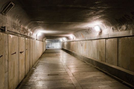 Old abandoned underground tunnel partly illuminated with lamps