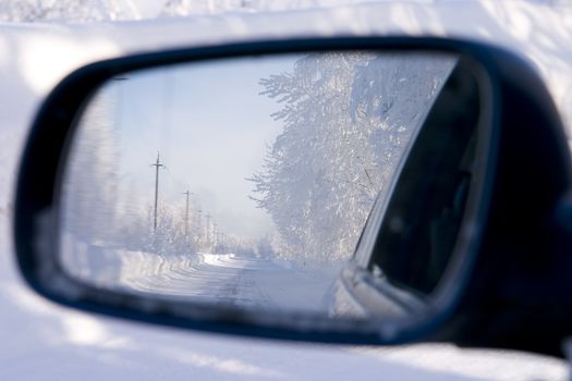 Winter fantastic wood and the lonely road, reflected in an automobile mirror of a back kind