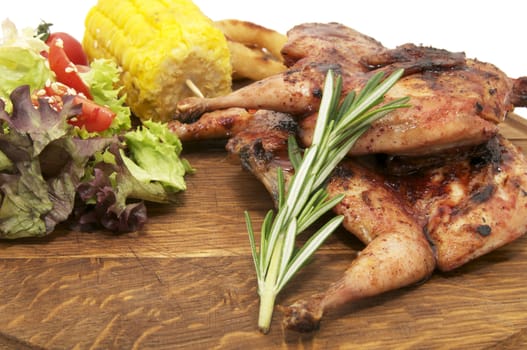 Grilled quail and vegetables on wooden plate