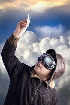 Boy as an old style pilot holding a toy airplane, heaven background