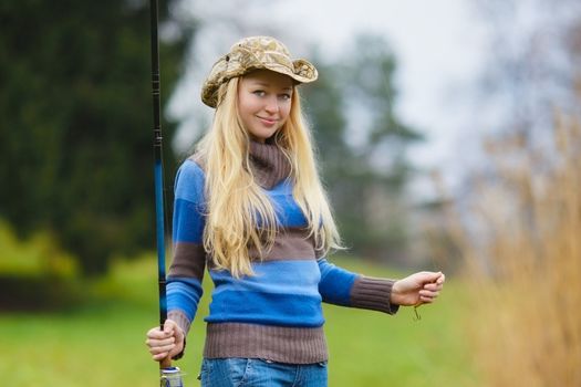 beautiful blond girl fishing in pond at autumn