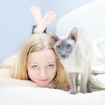 beautiful blond girl playing with cat in a bed