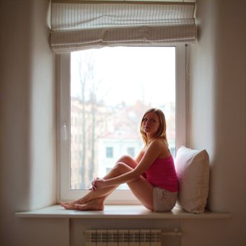 beautiful blond girl sitting on window sill