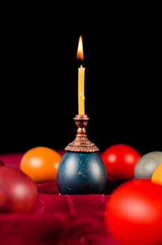 Candle standing on easter egg placed with many others on fabric