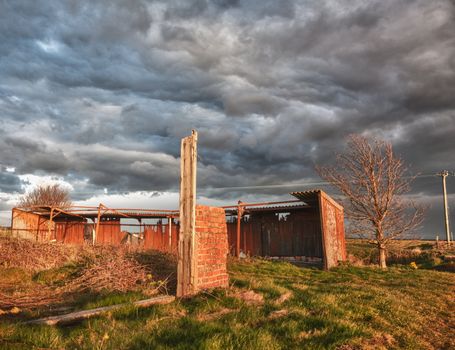Storm clouds over sunlit deserted and ruined barn on farmland