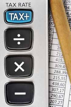 Detail of calculator, focusing the TAX key, next to a sheet of paper with numbers and a pencil.