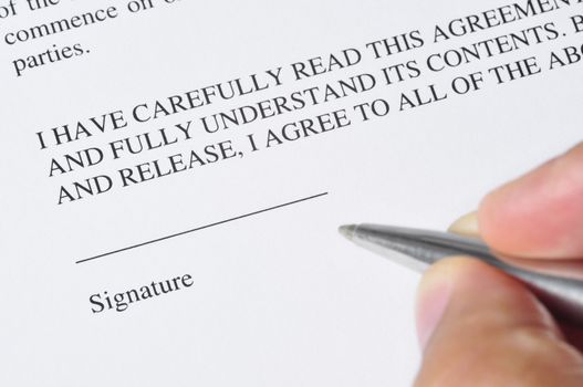 A hand, holding a pen, is ready to sign a document