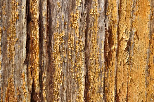 A wooden wall with it's yellow paint peeling off.