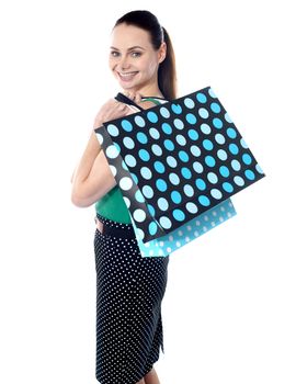 The attractive girl looks and smiles through a shoulder, holding in hands ditted shopping bags with purchases