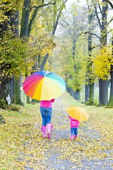 mother and her daughter with umbrellas in autumnal alley