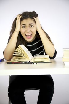 Girl studying book on a desk shouts desperate with hands in her long hair