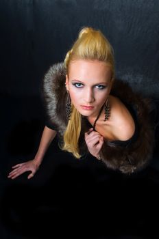 Young blond woman with fur, professional hair and makeup, on dark background. Focus on model's eyes.