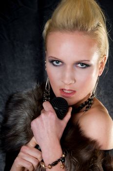 Young blond woman with microphone, fur, professional hair and makeup, on dark background. Focus on model's eyes.