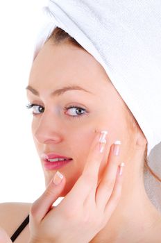 Young woman with white tower and nice manicure is appling cream on her face, on white background
