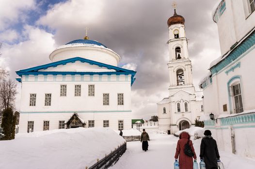 Scene of real life in a frosty winter day in Raifa monastery, near Kazan (Russia), where two women bring fresh water for their houses. In the background an orthodox priest and a visitor.