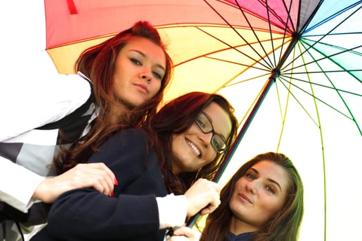 happy smiling girlfriends stay under colourful umbrella  