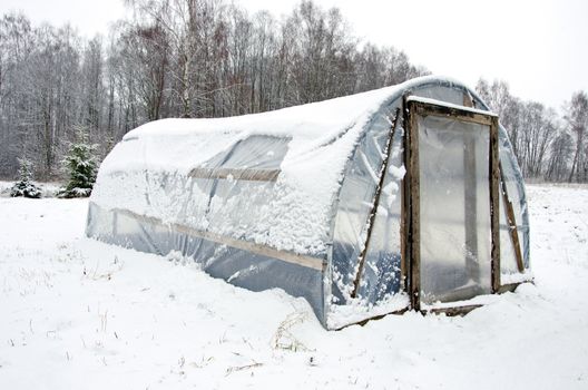 wooden diy homemade greenhouse covered with polythene and snow in winter.