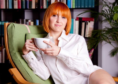 woman with red hair ist sitting on a chair and drinking coffee