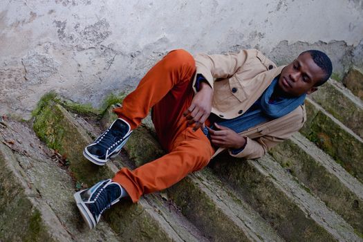 black man sitting on stairs outdoor with jacket and scarf