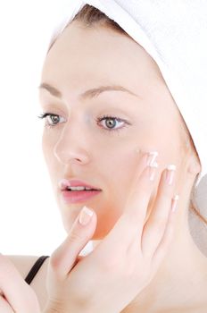 Young woman with white tower and nice manicure is appling cream on her face, on white background 