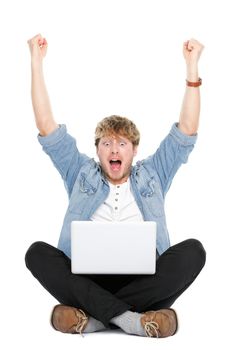 Man cheering with laptop computer and arms raised winning happy.  Young caucasian male model sitting on floor isolated on white background.