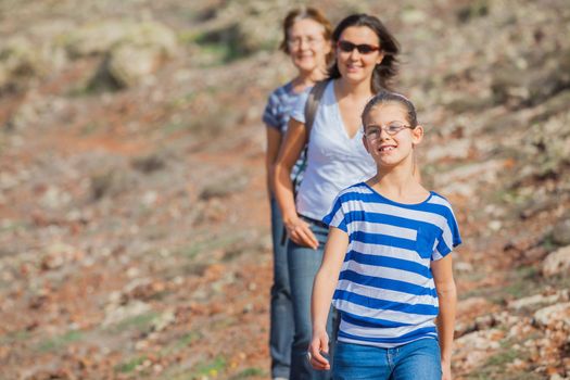 Family of three - girl, mother and grandmother hiking in the cross-country