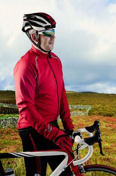 Cyclist standing and loooking to a beautiful green landscape with his bike.