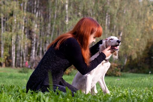 A girl in a black dress and white saliki pup in a forest 
