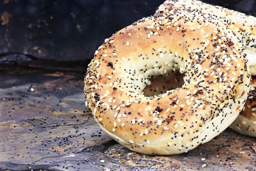 Stack of healthy bagels with sunflower meat and poppy seeds against a rustic slate background.

