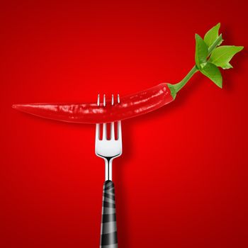 red hot chili pepper pierced by fork on red background .