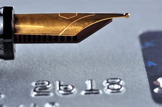 Closeup of a credit card with a golden fountain pen on top of it