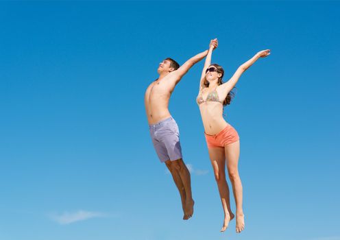young couple jumping together on a blue sky background