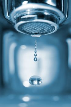 Water drop falling form a faucet in a blue bathroom, low depth of field
