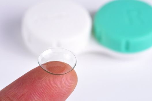 Contact lens on a finger tip with a lens case on the background