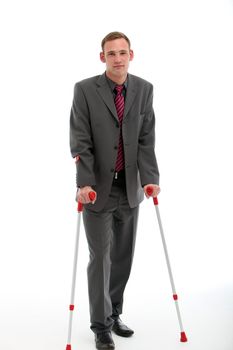 Smart young businessman in suit and tie walking with the aid of a pair of crutches, studio on white