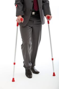 Lower body of a disabled or injured businessman walking on a pair of crutches, studio on white