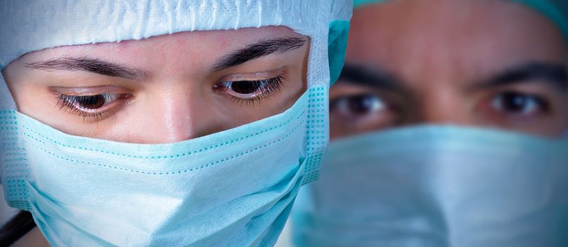 Closeup portrait of two surgeons during a surgery. Blue cast and vignetting applied. 