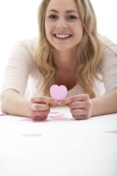 Smiling natural young blonde girl holding a pink paper valentine heart in her hand