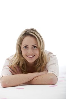 blonde woman wearing a light pink blouse lying on her stomach with her arms crossed in front of her on a white background