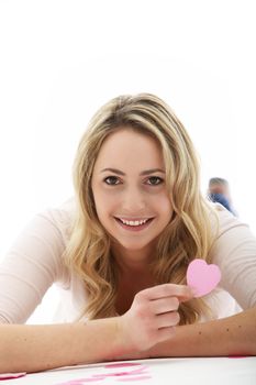 blonde woman holding a pink cardboard heart with her right hand in front of her