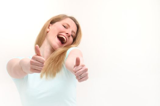 Enthusiastic laughing blonde woman giving thumbs up for success and approval isolated on white