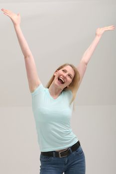 Pretty young blonde woman throwing her arms up into the air and laughing in jubilation at her success or victory