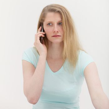 Worried woman sitting listening with a serious expression to bad news on her mobile phone