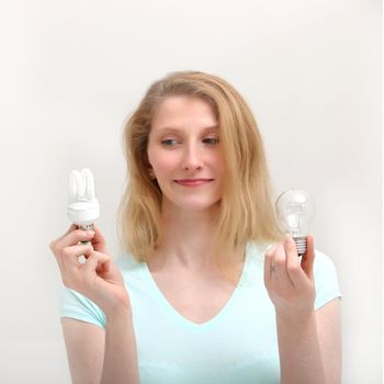 Pretty blonde woman holding two different light bulbs and eyeing the new eco-friendly spiral bulb with a smile as she makes her choice