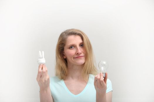 Woman holding a new spiral light bulb and an old incandescent one which she is eyeing with a look of condemnation